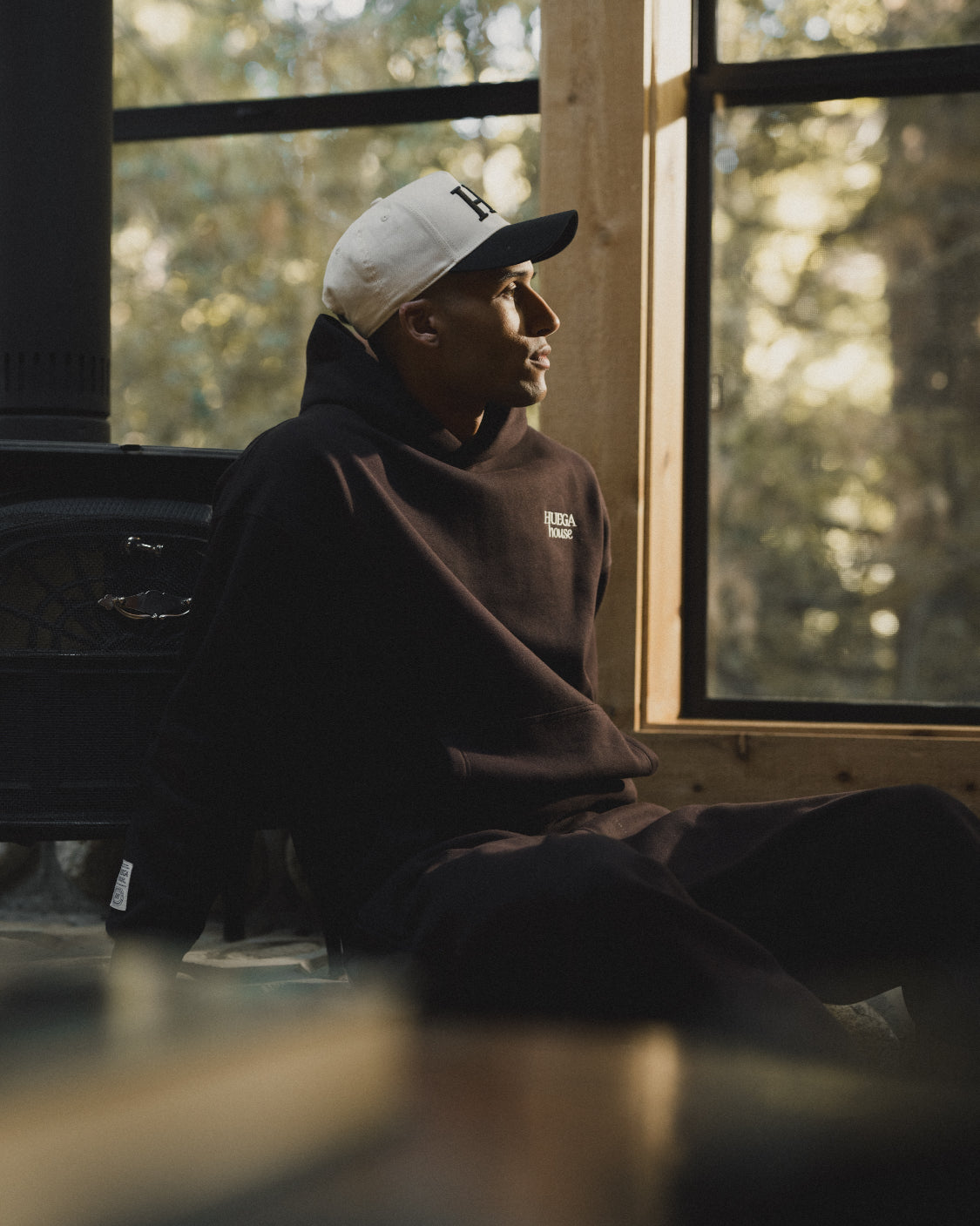 Person wearing a hoodie and cap sitting inside a vehicle with a window view of trees.