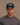 Person wearing a black cap and gray shirt with 'HUEGA' branding on a beige background